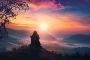 Silhouette of a woman sitting peacefully on a mountaintop at sunrise, symbolizing trust, rest, and God’s embrace.