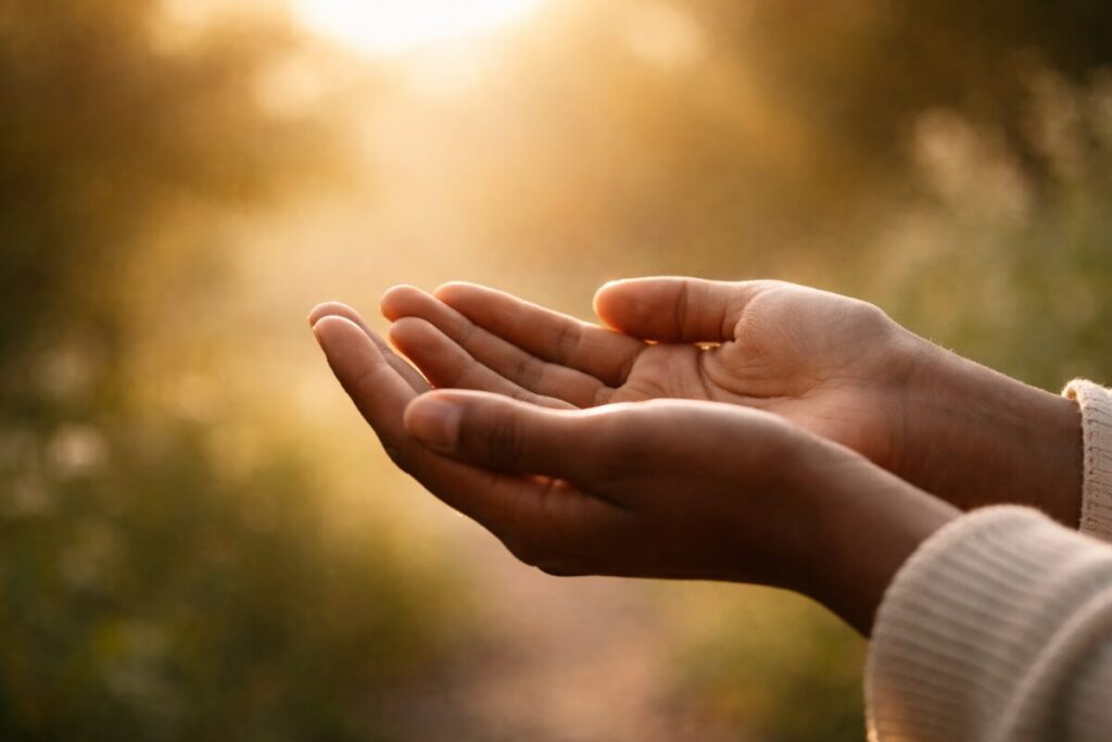 The open hands of a woman gently cupped and illuminated by warm, golden light, symbolizing trust, surrender, faith, and holding vision with openness.